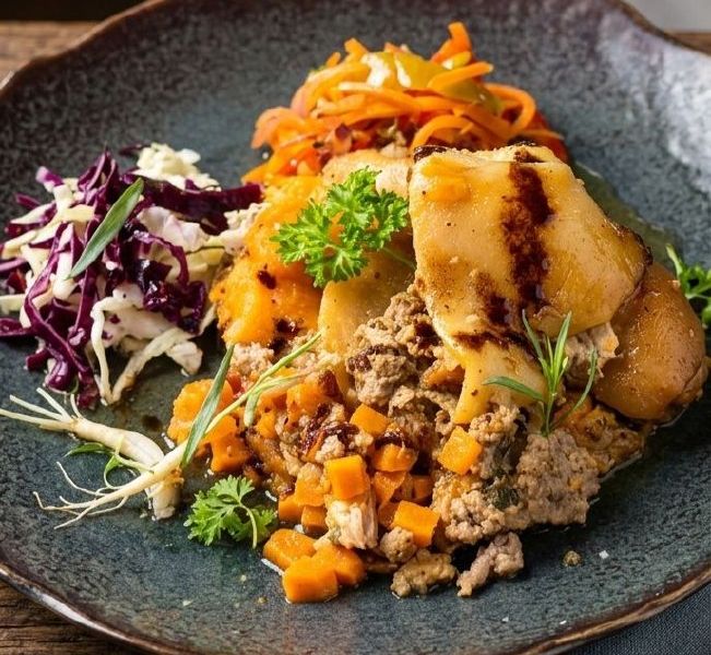 A plated catering dish: pulled meat and vegetables, glazed potatoes, red cabbage and carrots