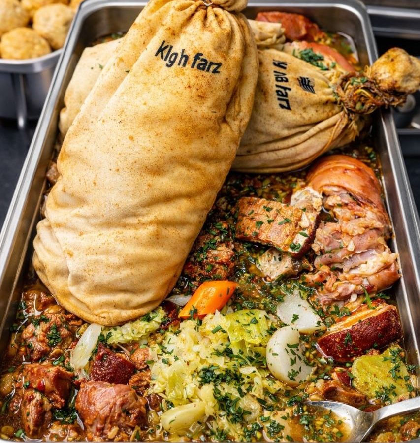 Kig ha farz in a gastro tray: two cloth-wrapped far, broth, meats, cabbage and potatoes, laid out for a catering buffet